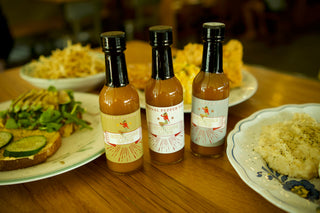 The Lady May Burning Love hot sauce trio of habanero, original and sweet pepper bottles on a brunch table, a gourmet small-batch farm-to-table Southern hot sauce gift idea