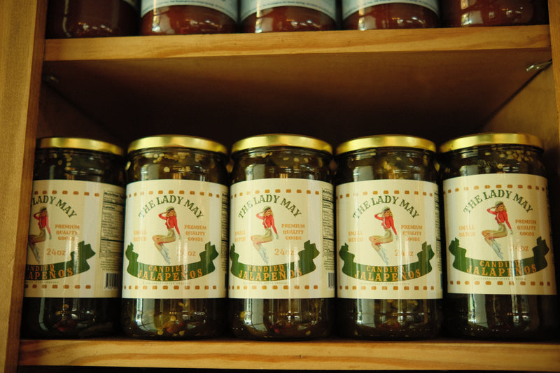 A row of The Lady May candied jalapenos 24oz jars on a wooden shelf, a gourmet traditional farm-to-table Southern pickled gift idea